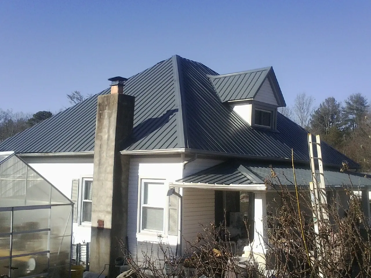 Dark blue standing seam metal roof on a white farmhouse with dormer — Slate & Tile Roof Repair by Roofing Brothers in Walworth